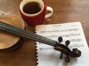 Violin and a cup of tea on sheet music, used to memorize fiddle tunes like the jig 'Tea & Tunes.'